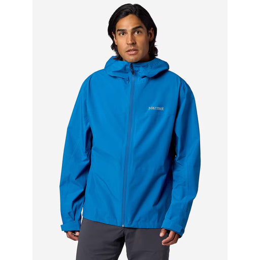 A man wearing a bright blue hooded jacket with a full front zipper and a small white 'marmot' logo on the left chest, paired with dark gray pants, against a light gray studio background.