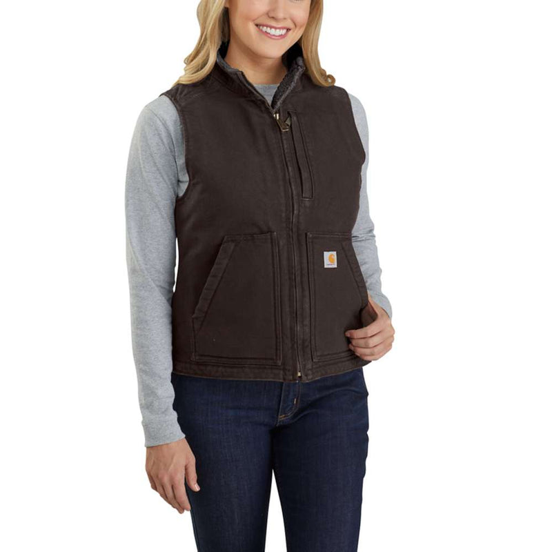 Happy woman wearing a dark brown colored sherpa-lined vest against a white background. The vest has one zipper pocket on the chest, as well as two pouch pockets towards the bottom. 