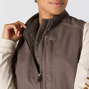Woman opening the collar of a taupe colored vest to reveal the interior sherpa lining.