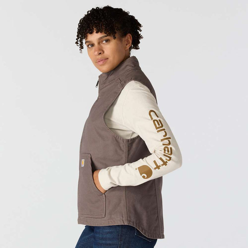 Side view of a woman wearing a taupe colored sherpa-lined vest with her hands in the pockets against a white background. 