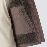 Taupe colored sherpa-lined vest being opened to reveal an interior zipper pocket. The pocket is surrounded by sherpa lining.
