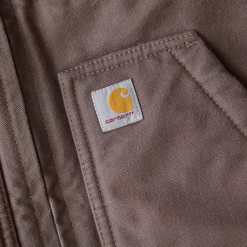 Close up of one of the pockets of a taupe colored vest with a Carhartt logo at the top of it. 