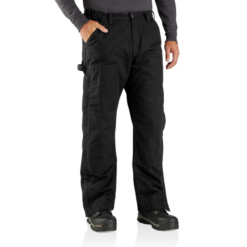 Man wearing loose fitting black work pants with his hand in one of the pockets against a white background.