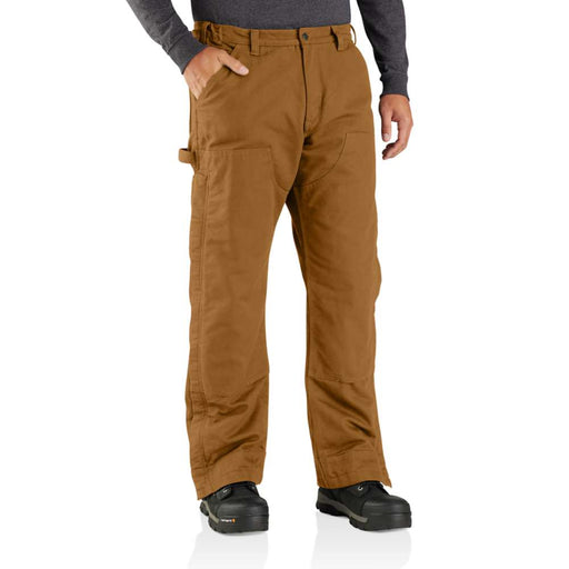 Man wearing loose fitting light brown work pants with his hand in one of the pockets.  