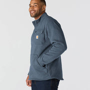Side-view of a happy man wearing a faded navy colored fleece jacket with chest pocket and Carhartt logo against a white background 
