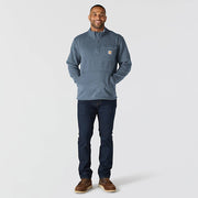 Happy man wearing a faded navy colored fleece jacket with Carhartt logo and chest pocket against a white background. The jacket comes down to his waist and has a pouch pocket with zippers towards the bottom.