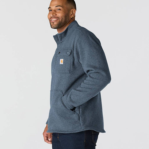 Side-view of a happy man wearing a faded navy colored fleece jacket with chest pocket and Carhartt logo against a white background 