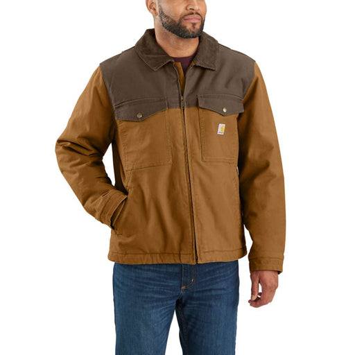 Man putting his hand in the pocket of a brown colored duck-lined insulated jacket against a white background. The jacket also has two other pockets higher up on the chest with the right side pocket having a Carhartt logo on it.