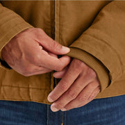 Man pulling down the sleeves of a brown duck lined insulated jacket. 