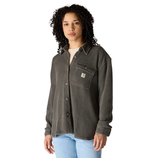 A woman wearing a dark gray Carhartt waffle-knit button-up shirt with a small orange brand patch on the chest pocket, paired with light blue jeans, against a plain white background.