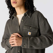 A person wearing a dark gray waffle-knit button-up overshirt with a visible Carhartt logo patch on the chest pocket, layered over a light cream shirt. The photo is a close crop showing the upper body and hands against a plain light gray background.