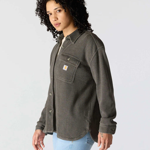 A model wearing a dark gray Carhartt waffle-knit button-up shirt with a chest pocket and the signature Carhartt logo patch, paired with light blue jeans against a light gray studio background.