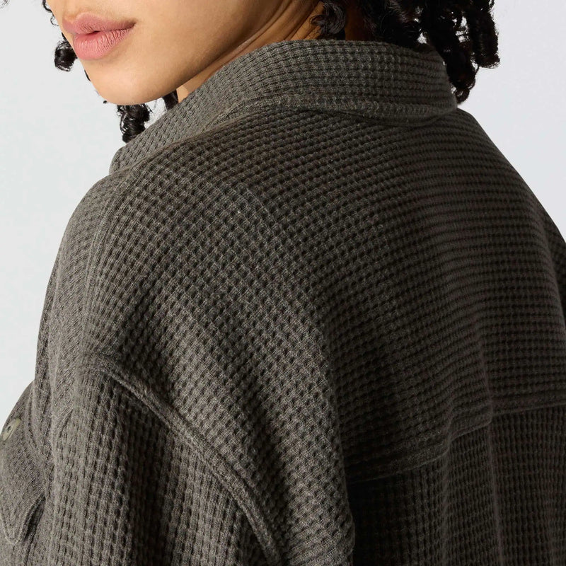 Close-up of a person wearing a dark gray waffle-knit overshirt, showing the textured fabric and collar detail against a light gray background.