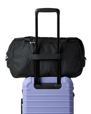 A black duffel bag on top of a purple luggage bag