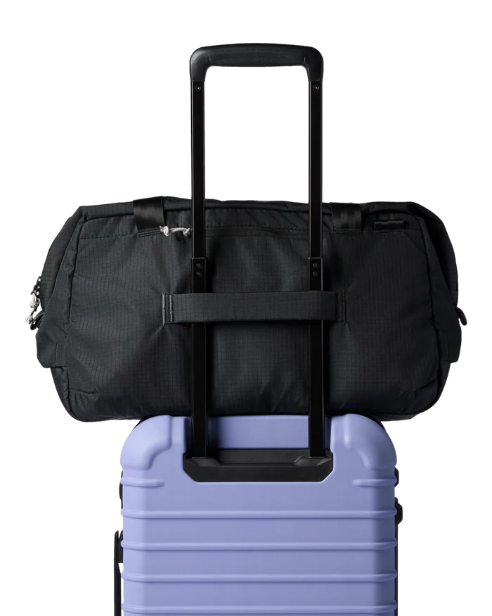 A black duffel bag on top of a purple luggage bag