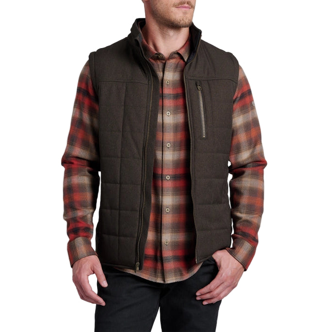 Man wearing a brown vest over a plaid shirt on a white background