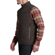 Man wearing a dark brown quilted vest over plaid sleeves on a white background