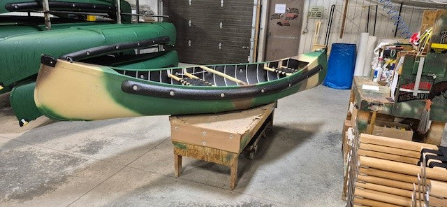 Side view of a green and tan colored canoe sitting on a table in a warehouse against a white background. 