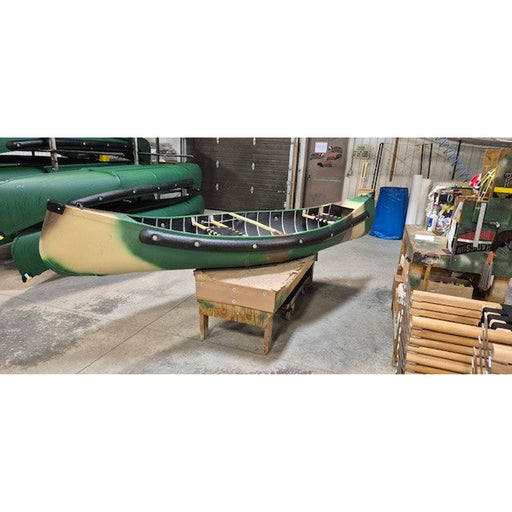 A green and beige canoe resting on a wooden stand inside a workshop or garage, with other boats and equipment visible in the background.
