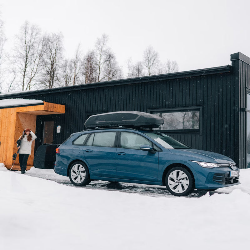 Woman walking out to her car in the snow. The car has a black cargo roof rack attached to the top of it. 