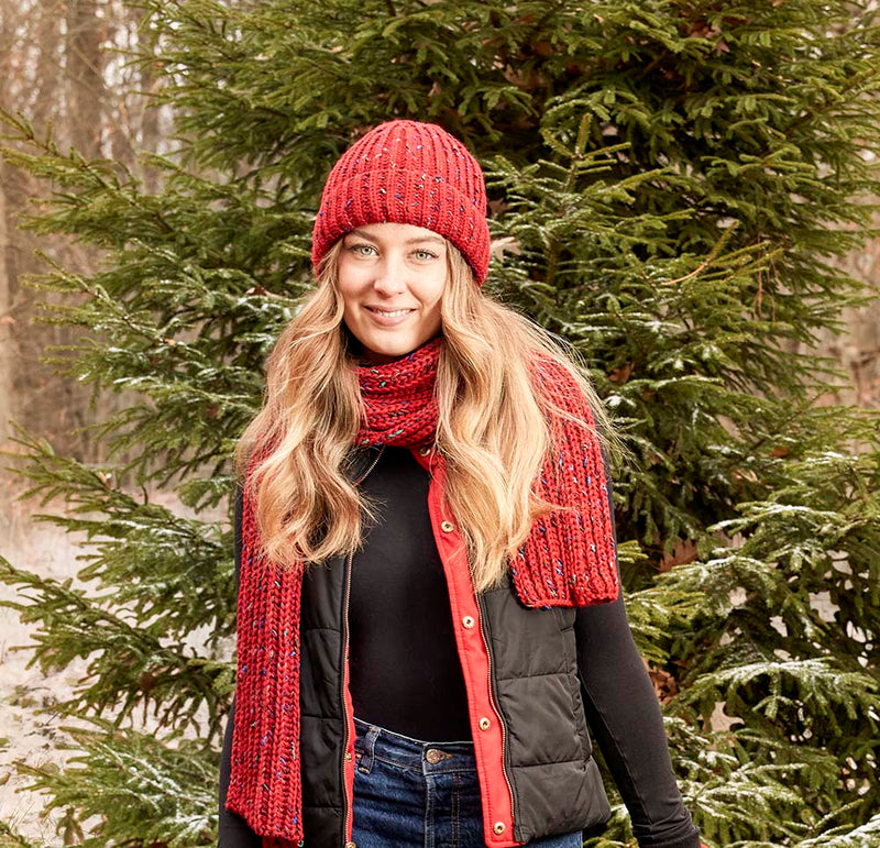 Woman wearing a red knit beanie hanging out in the woods. 