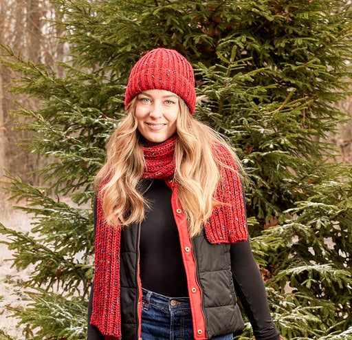 Woman wearing a red knit beanie hanging out in the woods. 