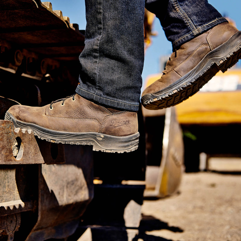 Person wearing brown work boots and blue jeans standing on a piece of heavy machinery.