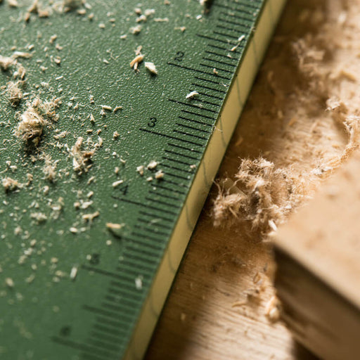 Close-up of a green ruler stamped on the edge of a notebook cover on a wooden surface with wood shavings.