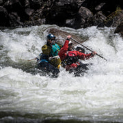 Man and woman white water kayaking with rocks in the background.