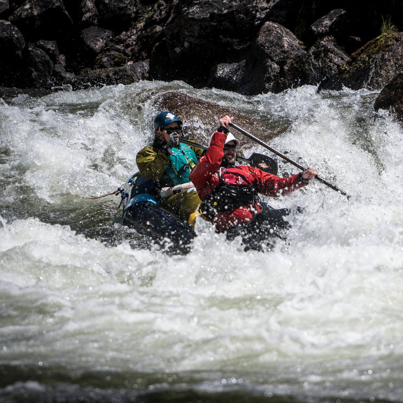 Man and woman white water kayaking with rocks in the background.