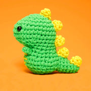 Green and yellow crocheted dinosaur toy on an orange background