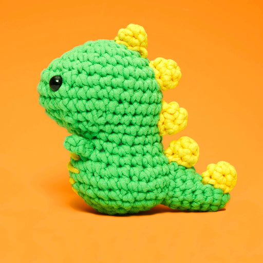 Green and yellow crocheted dinosaur toy on an orange background