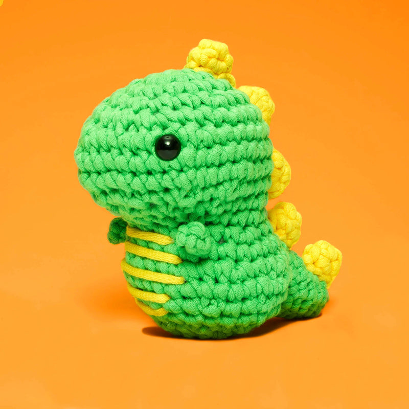 Green and yellow crochet dinosaur toy on an orange background