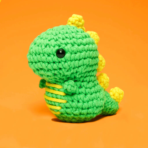 Green and yellow crochet dinosaur toy on an orange background