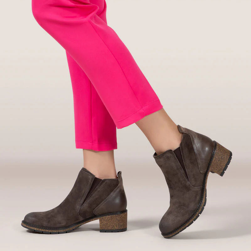 Side view of a woman wearing a pair of dark brown ankle boots against a white background. 