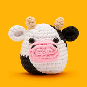 Crocheted cow toy with a pink nose on an orange background
