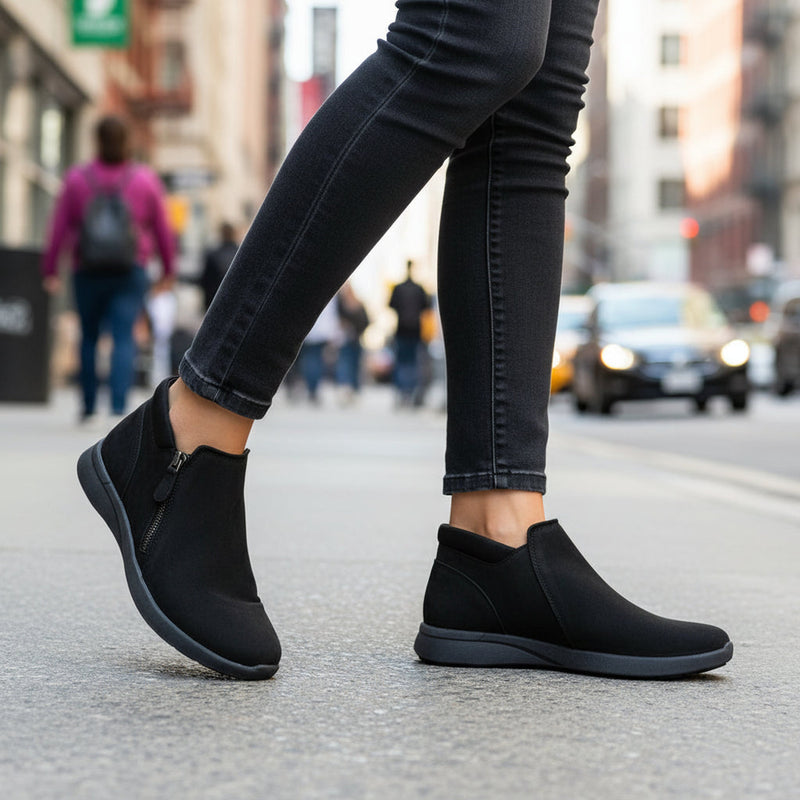 Side view of a woman walking down a crowded street wearing a pair of black ankle shoes.