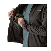 A close-up of a person wearing a black Patagonia zip-front jacket over a muted blue-green shirt, opening the jacket to show a side pocket containing an olive green pouch.