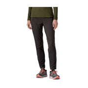 A person from the waist down wearing slim-fit black athletic pants, an olive green long-sleeve top, and black trail running shoes with coral accents, set against a plain white background.