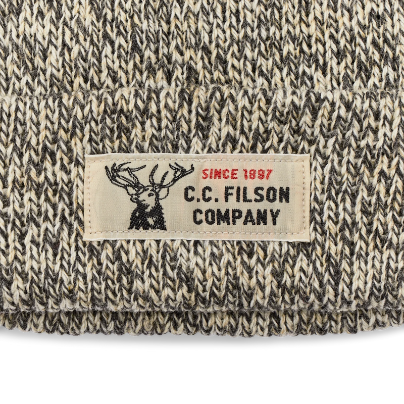 Close up of a white beanie with black accents featuring a Filson logo against a white background. 