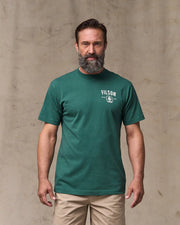 Man wearing a green Filson t-shirt against a beige background