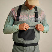 Man opening the zipper pocket of his sage colored waders. 