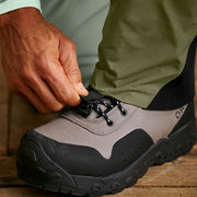 Man adjusting the strap on his gray and black hiking boot. 