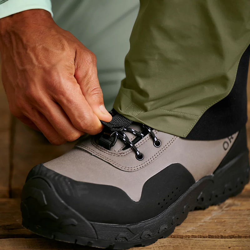 Man adjusting the strap on his gray and black hiking boot. 