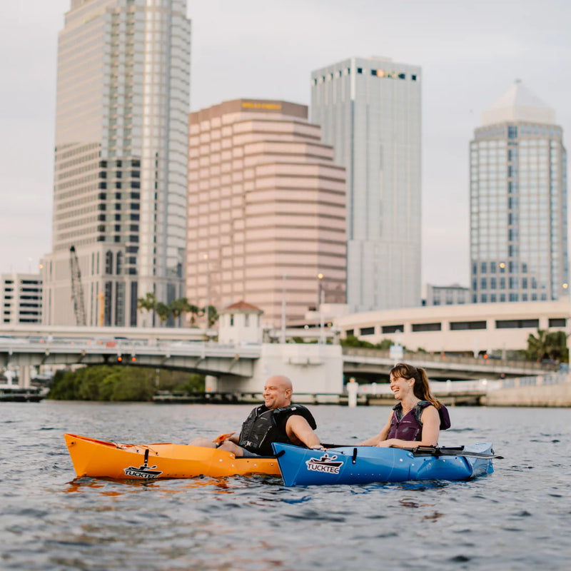 Two people kayaking on water with city skyline in the background