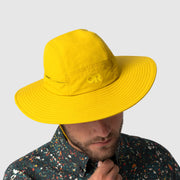 Person wearing a yellow hat with a brand logo on a light gray background