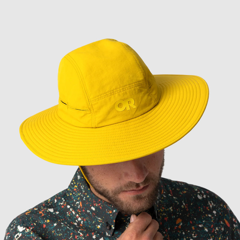Person wearing a yellow hat with a brand logo on a light gray background