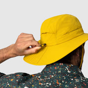 Person adjusting a yellow bucket hat against a plain background
