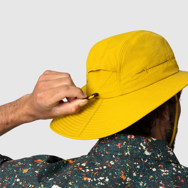 Person adjusting a yellow bucket hat against a plain background