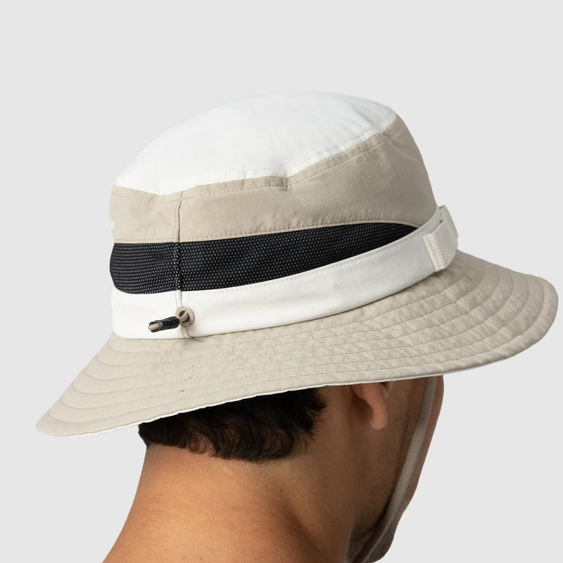 Beige bucket hat with a black mesh band worn by a person on a white background